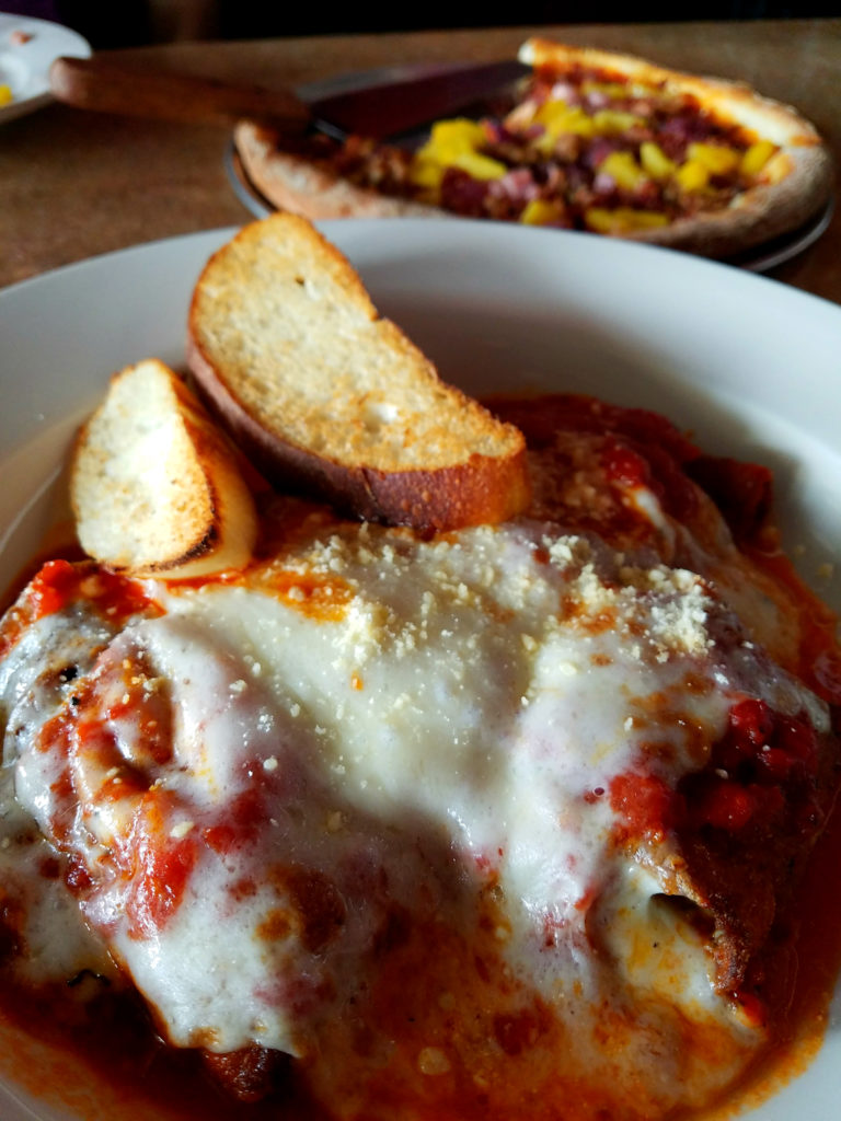 Delicious baked Italian classic with bubbling cheese and sauce on plate. Pizza blurred in the background.